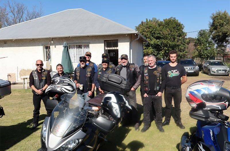 A group of bikers standing behingd a black motorcycle