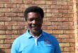 Black man wearing a light blue ACDP shirt standing in front of a brick wall