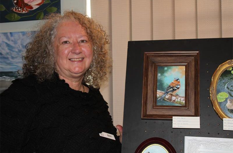 Woman with curly hair standing next to miniature frmaed paintings