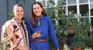 Two white women stand next to a herb garden holding sheers