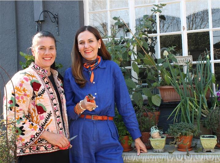 Two white women stand next to a herb garden holding sheers
