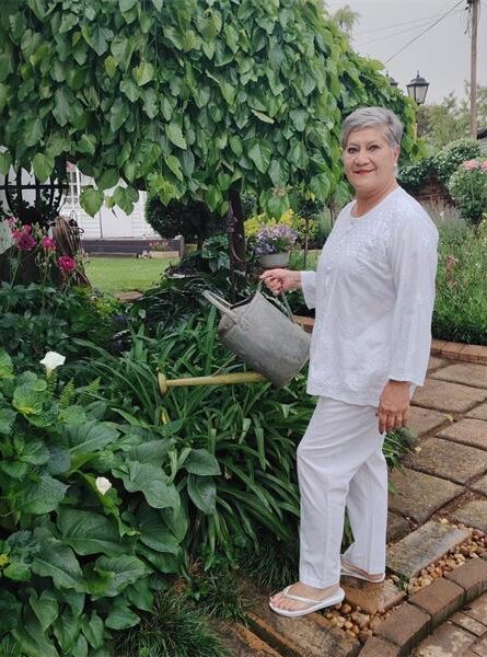 Grey haired woman wearing white holding a watering can