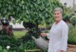Grey haired woman wearing white holding a watering can