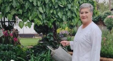 Grey haired woman wearing white holding a watering can