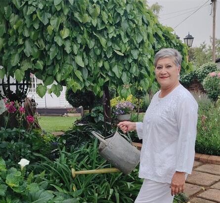 Grey haired woman wearing white holding a watering can