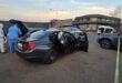 Two people wearing PPE standing next to two cars