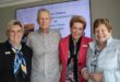 Three women smiling standing next to a man