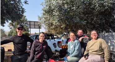 Two men standing next to a quad bike with three women sitting on top