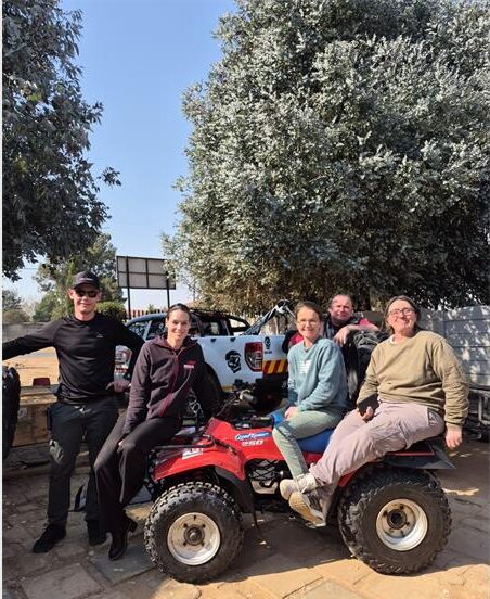 Two men standing next to a quad bike with three women sitting on top