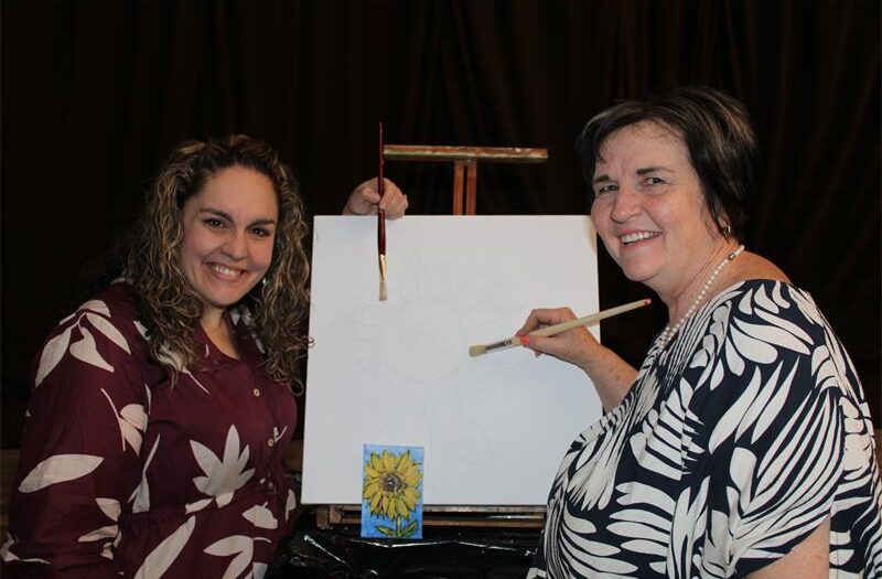 Two women holding paintbrushes to a canvas