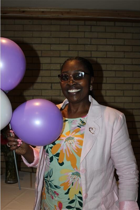 Black woman wearing a floral dress holding white and purple balloons