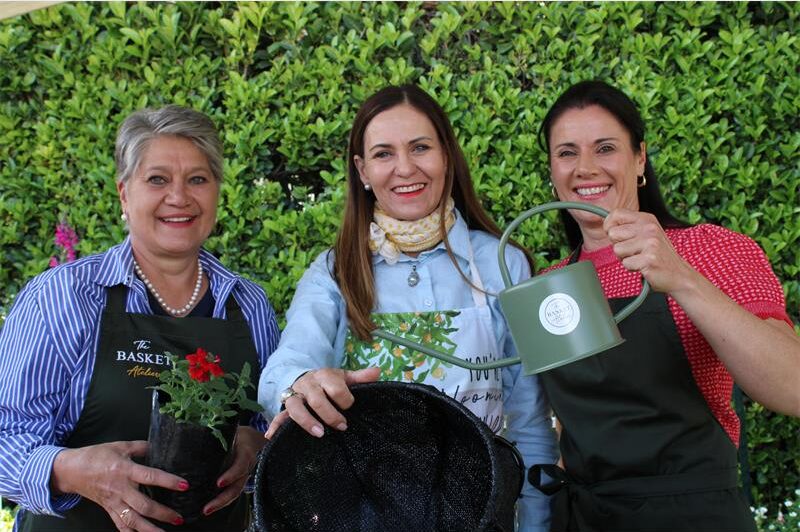 Three women posing with plants, a watering can and hanging basket