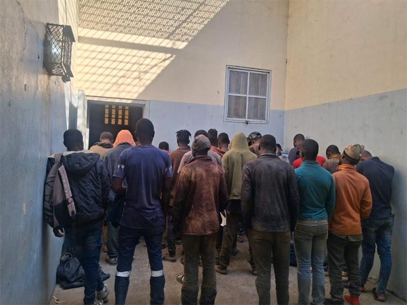 A GROUP OF MEN STANDING AND FACING HOLDING CELLS WALLS