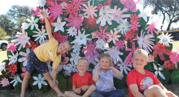 Four kids, a girl and three boys doing playful poses in front of a spring display