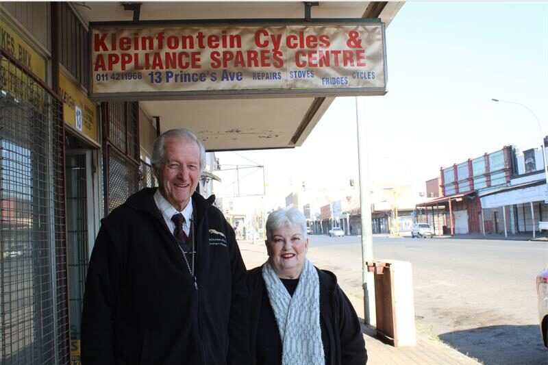 An elderly man and women stand next to a street under a weather-worn sign