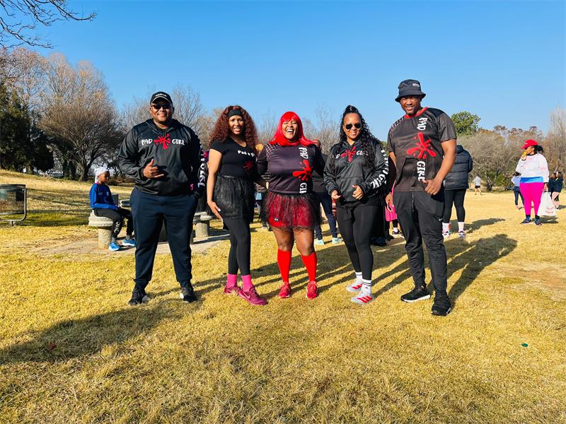 Two black men and three black women mainly dressed in black standing on grass in a row. 