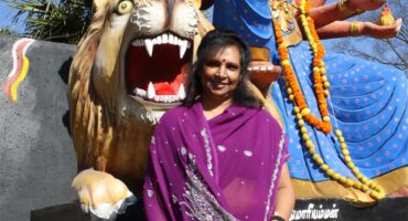 Indian woman wearing a purple sari sitting in front of a religious statue