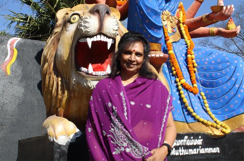 Indian woman wearing a purple sari sitting in front of a religious statue