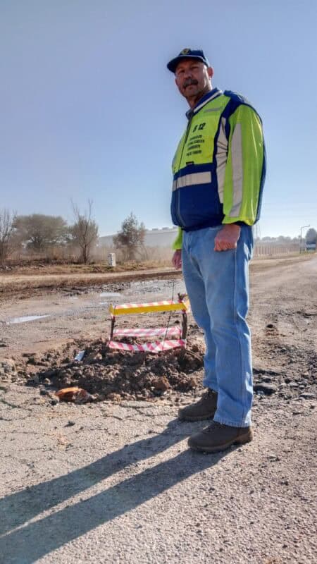 Man wearing a reflective jacket standing at a pothole