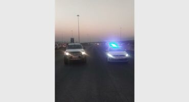 Two vehicles with headlights on facing the camera and parked on a highway.