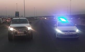 Two vehicles with headlights on facing the camera and parked on a highway.
