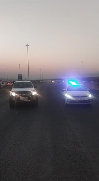 Two vehicles with headlights on facing the camera and parked on a highway.