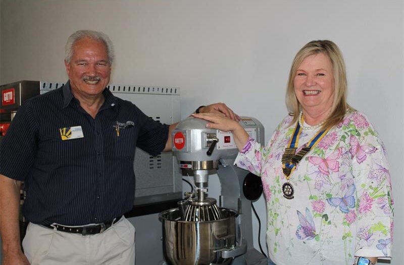 Man and woman smiling as their hands rest on an industrial cake mixer
