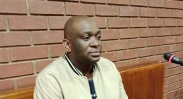 Black man staring out in front of him while sitting in a court's witness stand