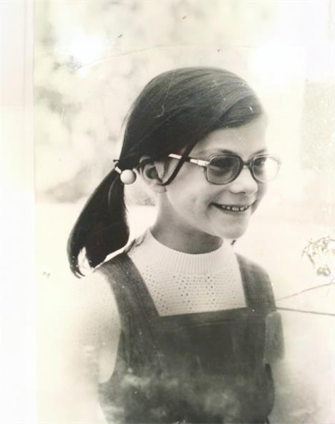 A black and white photo of a young girl with pigtails and glasses.