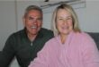 Man smiles as he sits next to a woman wearing a pink robe