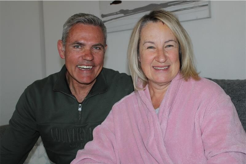 Man smiles as he sits next to a woman wearing a pink robe