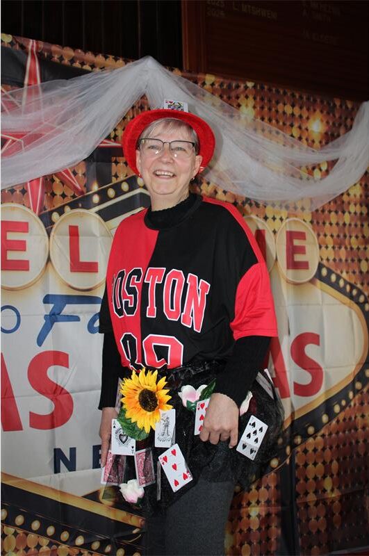 Elderly white woman smiles while wearing tutu adorned with playing cards