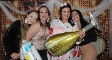 Four white women smile holding balloons shaped as a champaign bottle and diamond ring