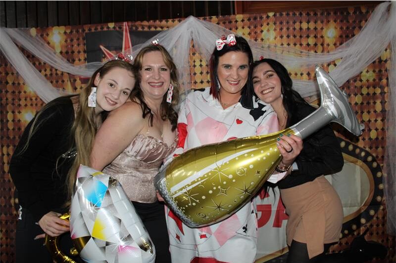 Four white women smile holding balloons shaped as a champaign bottle and diamond ring