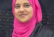 A head and shoulders photo of an Indian woman wearing a black dress and pink headscarf.
