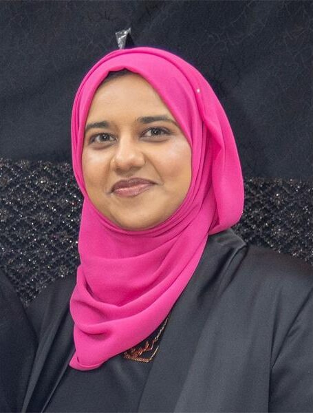 A head and shoulders photo of an Indian woman wearing a black dress and pink headscarf.
