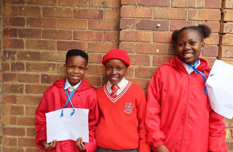 Three learners standing next to each other in red uniform