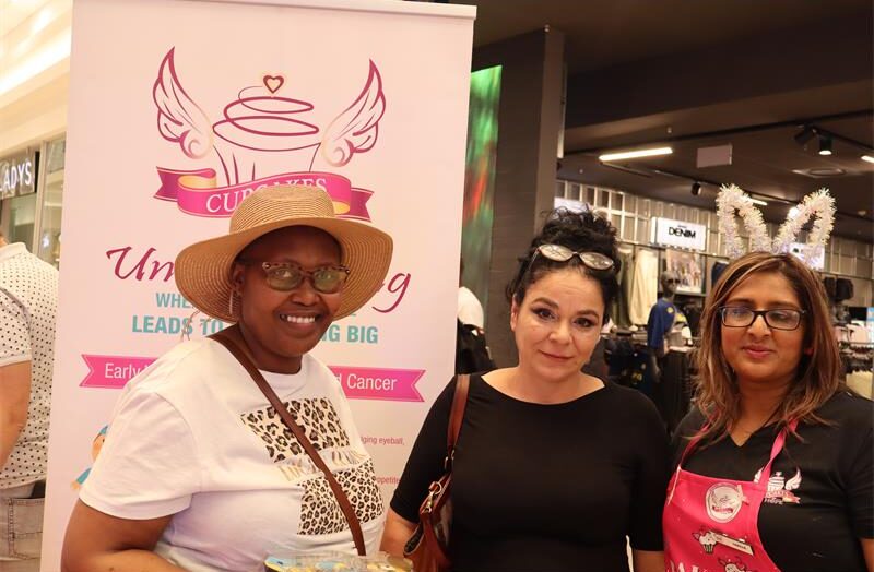 Three ladies standing next to each other in front of a pink banner