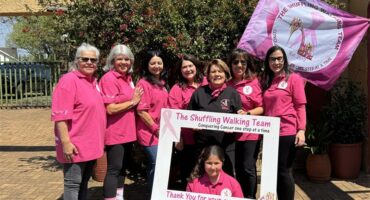 Group of women dressed in pink, holding a banner and photo frame