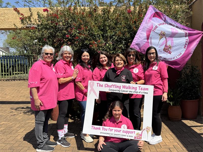 Group of women dressed in pink, holding a banner and photo frame