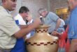 Man wearing a blue cap talking to another while resting his hand on a wooden pot