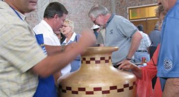 Man wearing a blue cap talking to another while resting his hand on a wooden pot