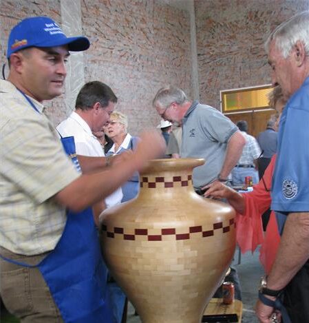 Man wearing a blue cap talking to another while resting his hand on a wooden pot