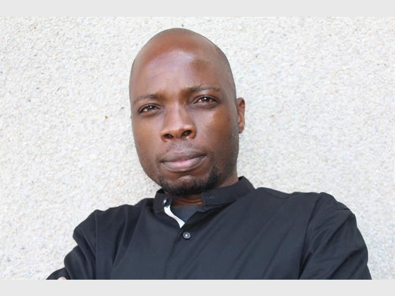 A head and shoulders photo of a black male with a shaved head wearing a black shirt looking at the camera.