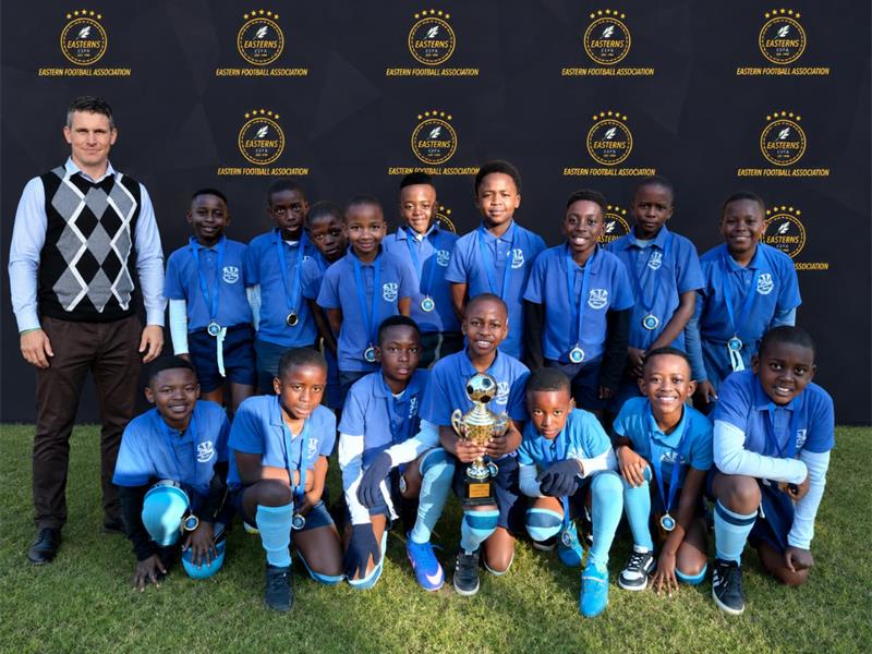 Group of boys in blue uniforms, holding a trophy and posing with a man