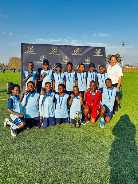 Group of boys in blue uniforms, holding a trophy and posing with a man
