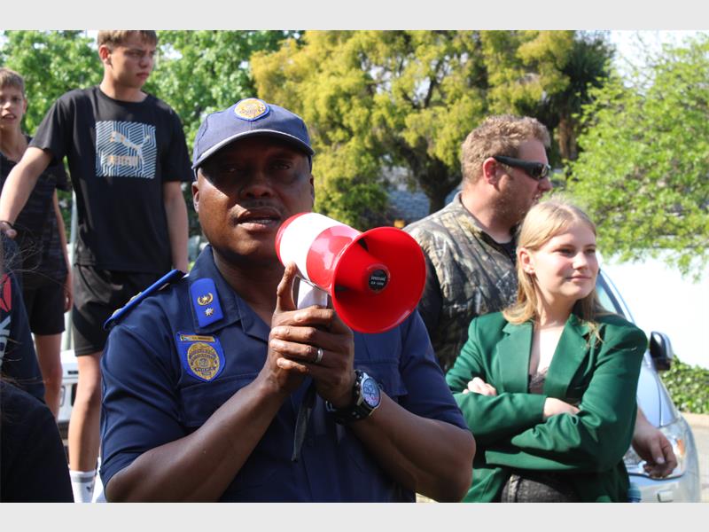 A member of the EMPD in uniform holding a megaphone with people in the background.