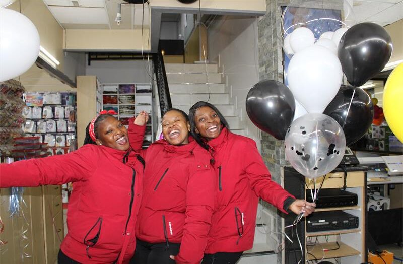 Three black women, dressed in red smile while holding balloons