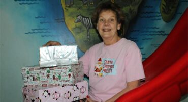 Woman wearing a pink shirt, sitting on a red slide holding gift boxes