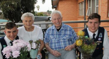 Twee jong seuns hou blomme aan bejaarde man en vrou